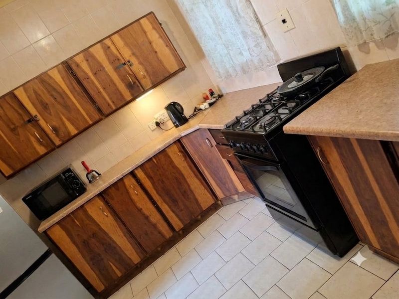 A functional kitchen featuring wooden cabinetry, laminate countertops, and a gas stove with tiled backsplash and flooring.