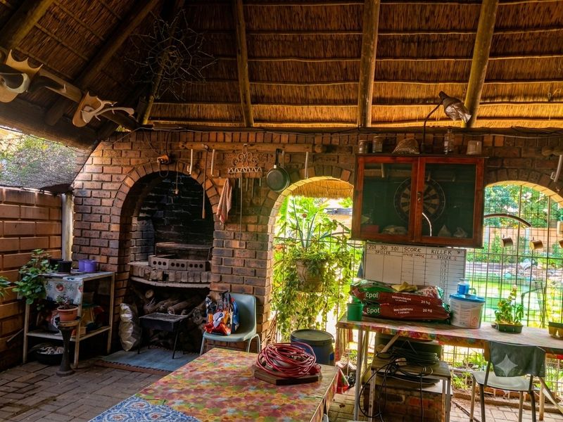 Covered outdoor entertainment area featuring a traditional thatched roof, exposed timber rafters, and a built-in brick braai fireplace.