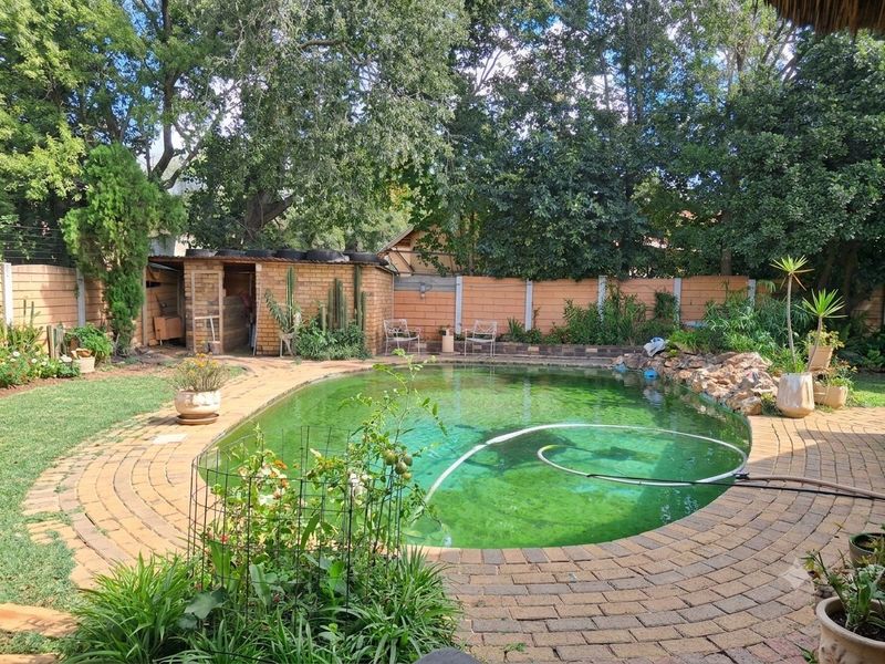 Outdoor pool area featuring a curved swimming pool, brick paving, and a brick boundary wall with an adjacent outbuilding.