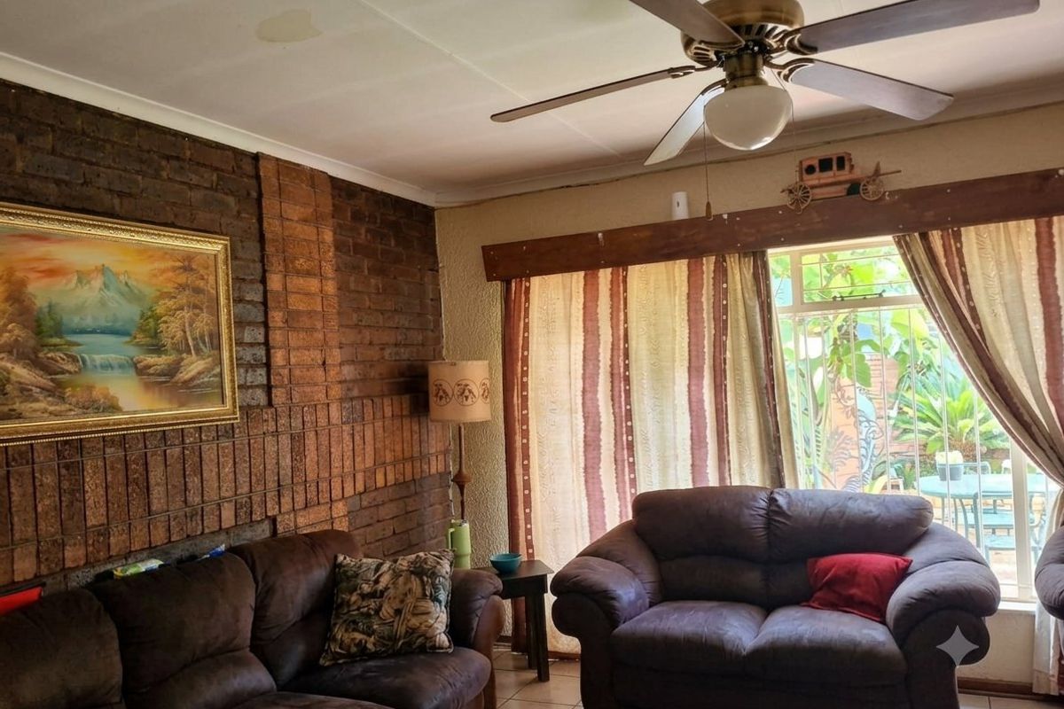 Living room featuring an exposed brick feature wall, tiled flooring, and a ceiling fan, with access to the outdoor area through a sliding door.