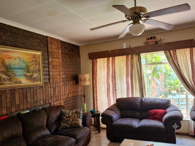 Living room featuring an exposed brick feature wall, tiled flooring, and a ceiling fan, with access to the outdoor area through a sliding door.