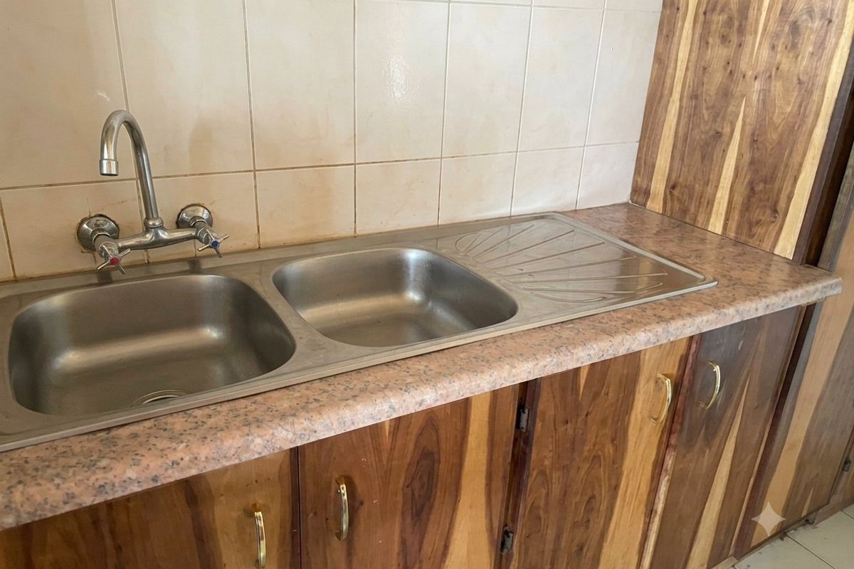 A functional kitchen area featuring a double bowl stainless steel sink, laminate countertops, and wooden cabinetry with a tiled backsplash.