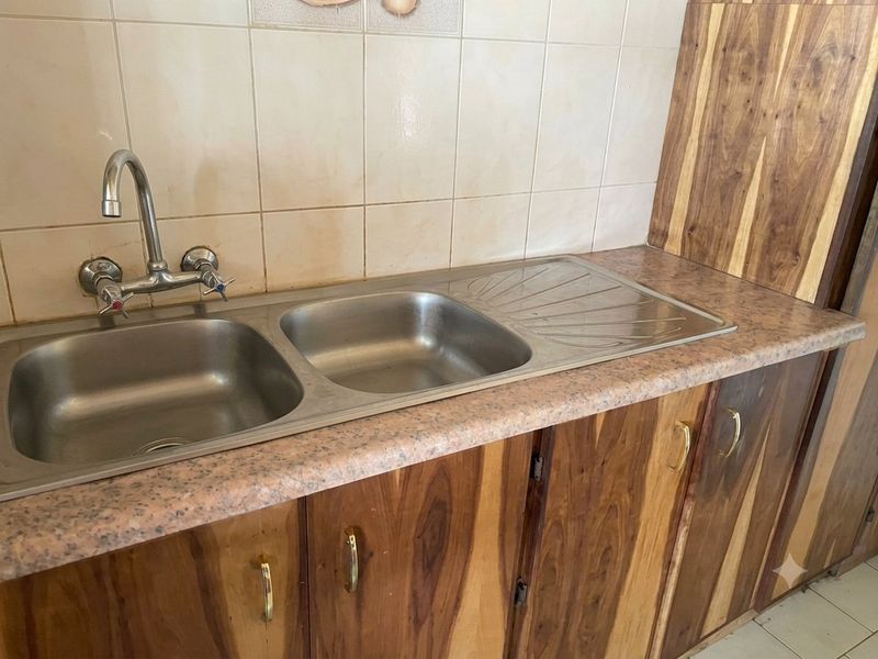 A functional kitchen area featuring a double bowl stainless steel sink, laminate countertops, and wooden cabinetry with a tiled backsplash.
