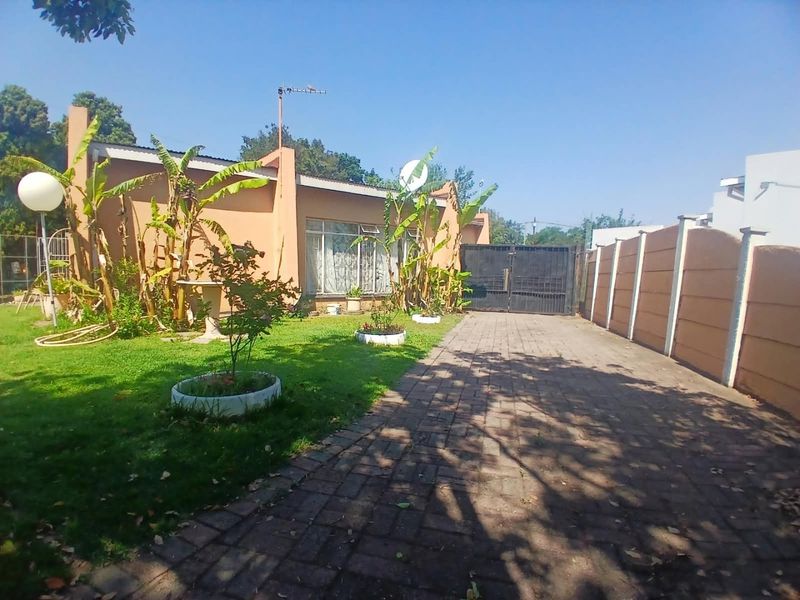 Front view of the property featuring a paved driveway, secure metal gate, and a precast concrete boundary wall with a landscaped garden area.