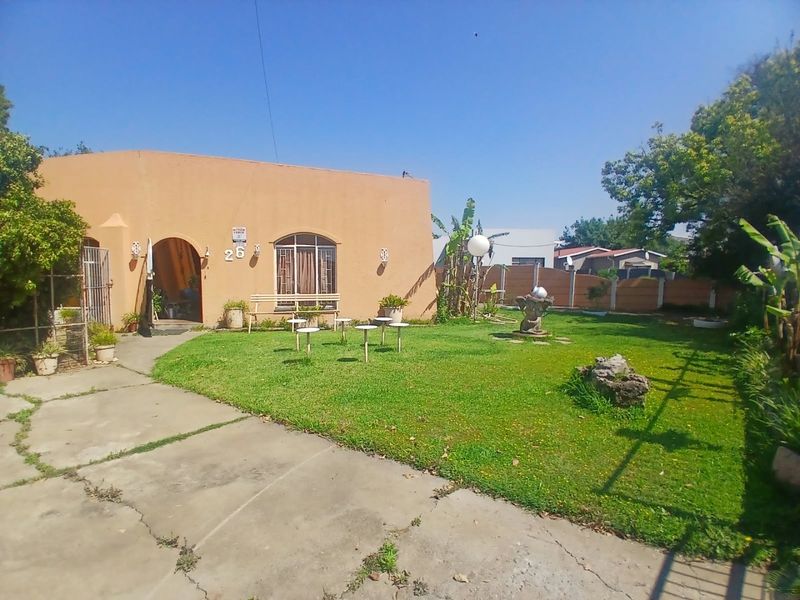 Front view of a single-story house featuring an arched entrance, arched window, concrete driveway, and a spacious front garden with boundary walling.