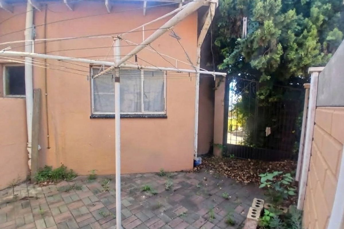 Rear exterior area featuring a paved courtyard, rotary clothesline, and gated access, showing signs of wear and maintenance requirements.