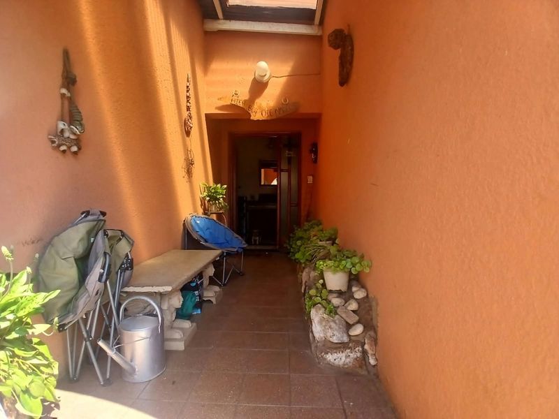 A covered outdoor patio area featuring tiled flooring, a translucent roof panel, and a stone-bordered planter bed along the wall.