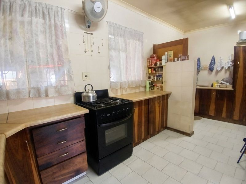 A functional kitchen featuring wooden cabinetry, laminate countertops, a gas stove, and tiled flooring, offering potential for a modern renovation.