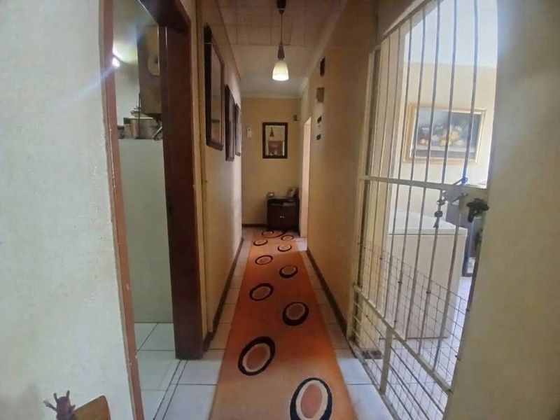 A narrow interior hallway featuring tiled flooring, a security gate, and pendant lighting, showing signs of wear and dated finishes.