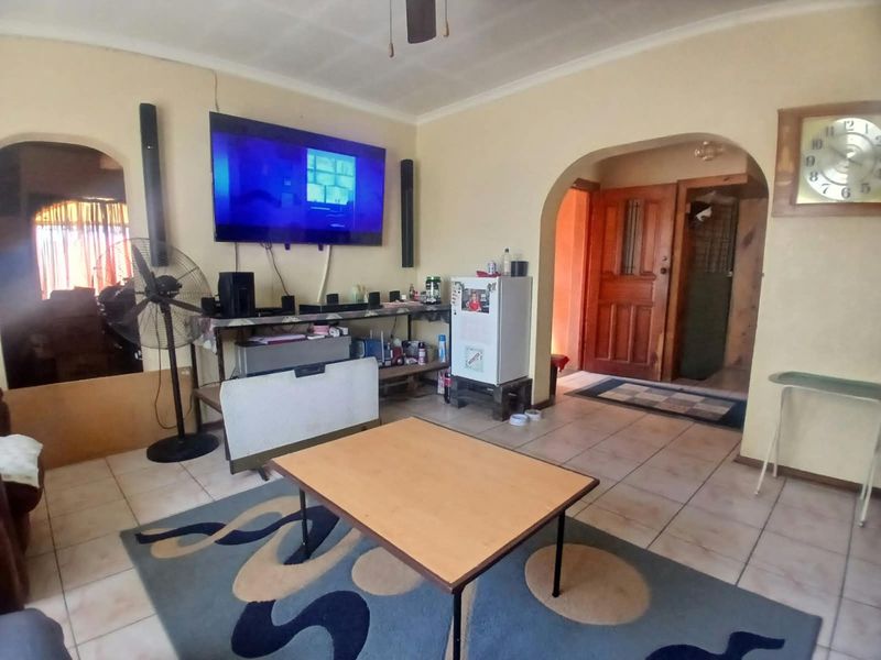 A living room featuring tiled flooring, arched doorways, and coved cornicing, offering a functional space with potential for cosmetic updates.