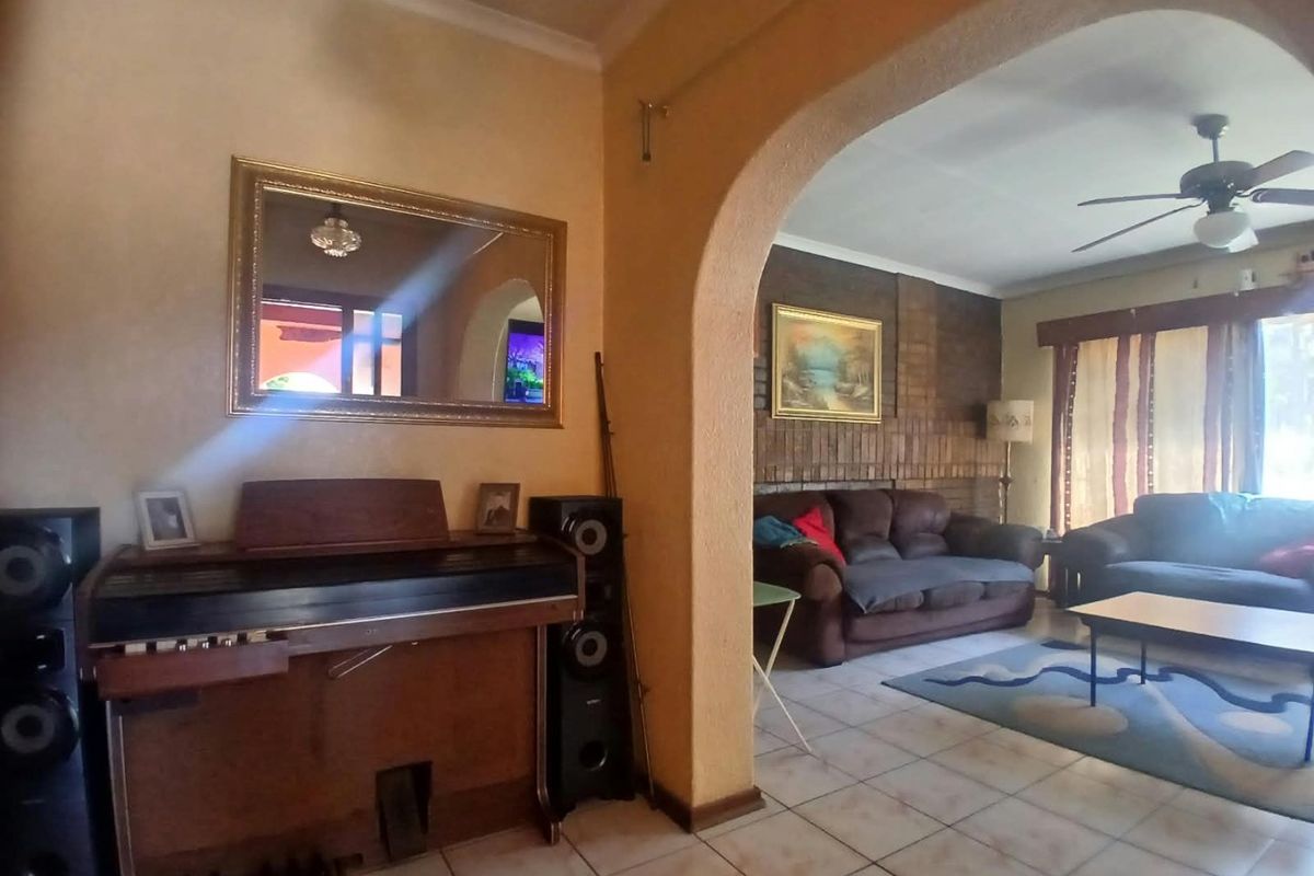 A living area featuring a brick accent wall, tiled flooring, and a decorative archway connecting to an adjacent space with a ceiling fan.