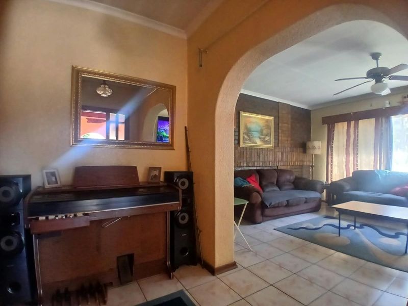 A living area featuring a brick accent wall, tiled flooring, and a decorative archway connecting to an adjacent space with a ceiling fan.