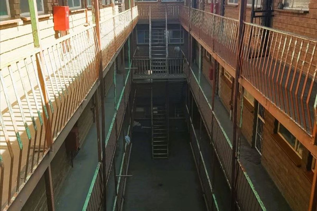 An exterior view of a multi-story residential building featuring open-air walkways, metal staircases, and brick facade construction.
