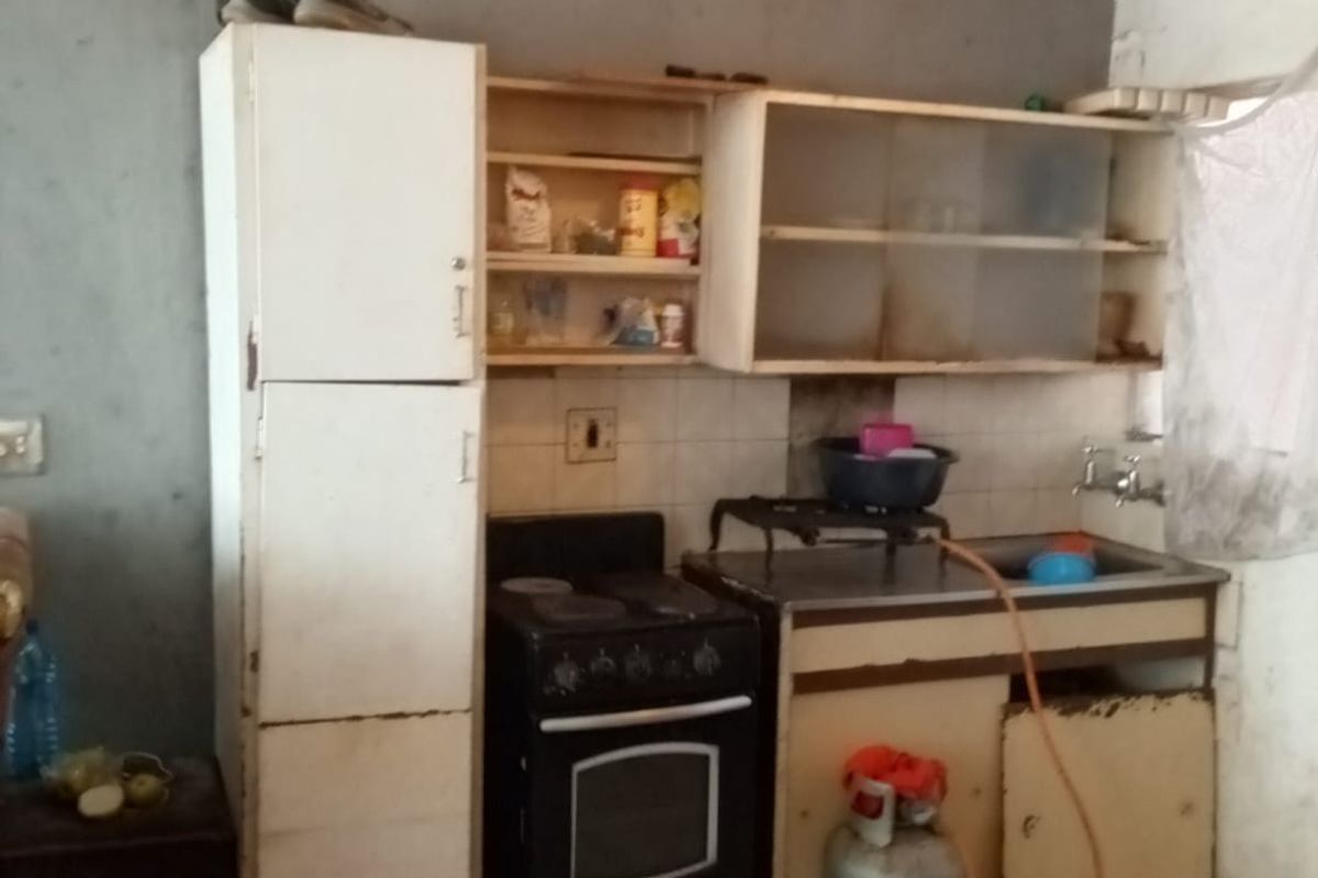 A dated kitchen area featuring basic cabinetry, a freestanding stove, and a stainless steel sink, requiring significant modernization and finish updates.
