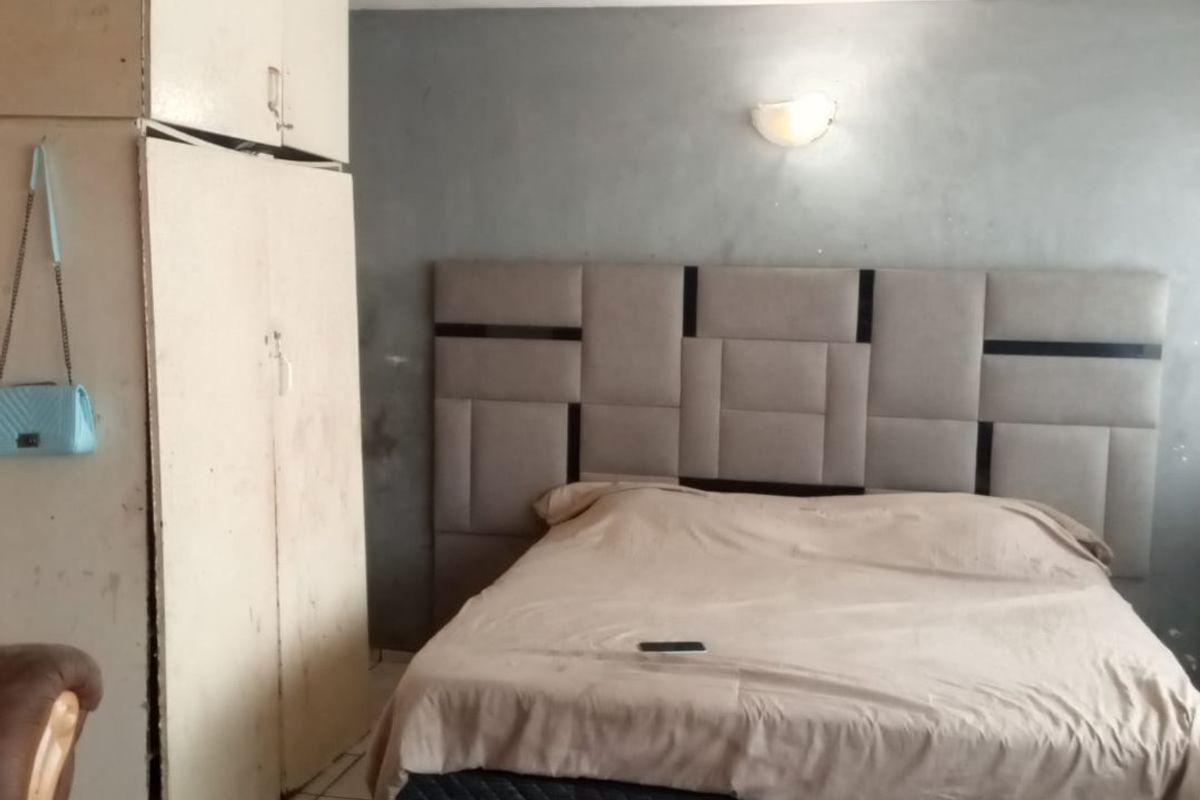 A bedroom featuring tiled flooring, a built-in wardrobe, and a grey accent wall with a mounted headboard.