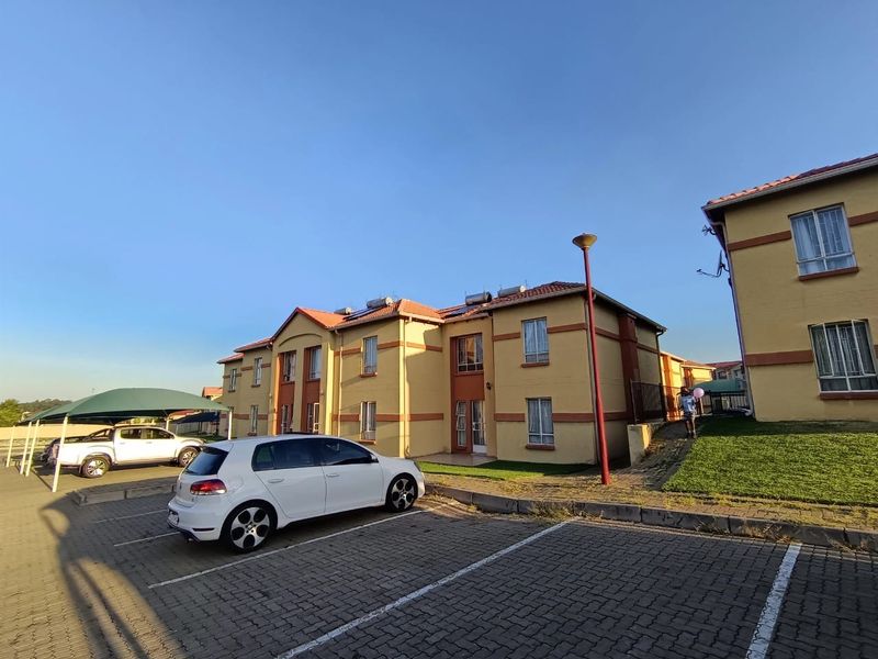 Exterior view of a townhouse complex featuring paved parking, a carport, and solar water heating systems on the tiled roof.