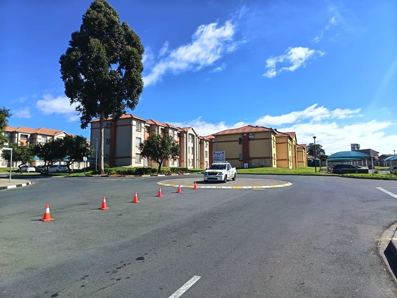 Exterior view of a townhouse complex featuring multi-story residential buildings, a paved roundabout, and landscaped grounds under a clear blue sky.
