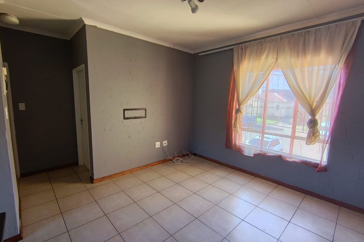 An empty living room featuring ceramic floor tiles, coved ceilings, and security bars on the window. The walls require cosmetic attention.