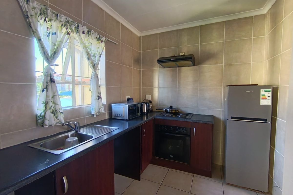 Functional kitchen featuring dark wood cabinetry, laminate countertops, tiled splashbacks, and integrated cooking appliances including an oven and hob.
