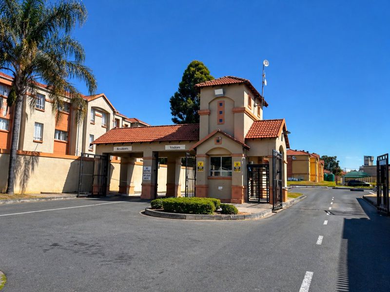 A well-maintained security gatehouse at the entrance of the townhouse complex, featuring separate access lanes for residents and visitors.