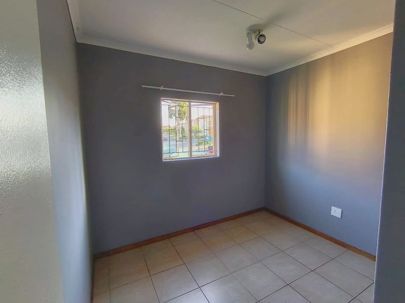A clean, empty bedroom featuring neutral grey walls, tiled flooring, and a window fitted with security bars.
