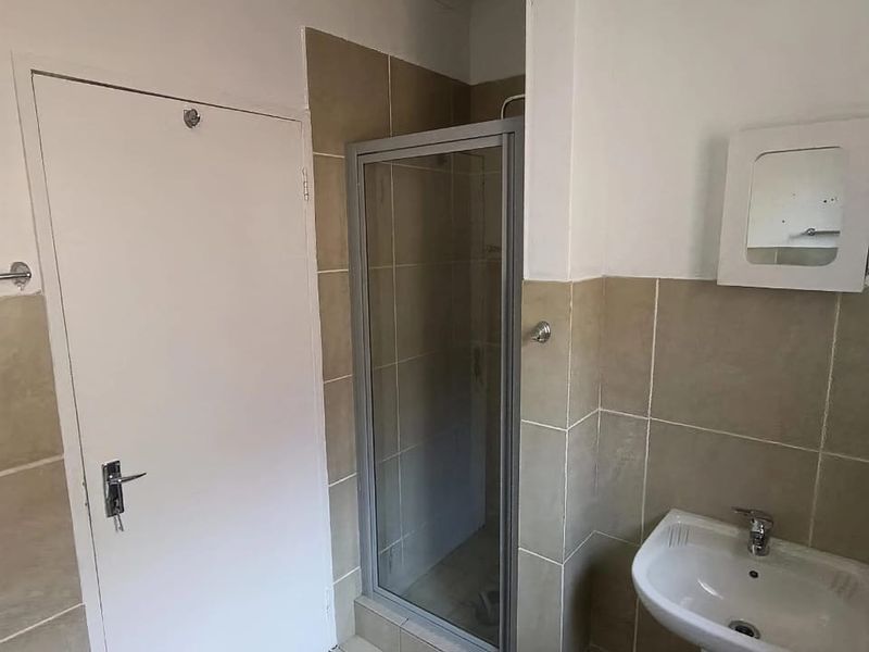 A functional bathroom featuring a pedestal basin, shower enclosure, and neutral wall and floor tiling, offering a blank canvas for modernization.