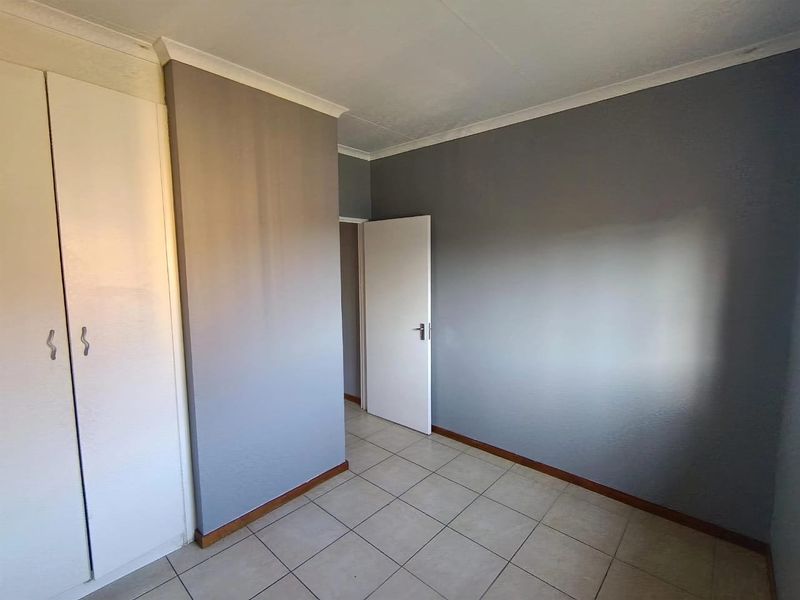An empty bedroom featuring tiled flooring, a built-in wardrobe, and neutral grey painted walls.