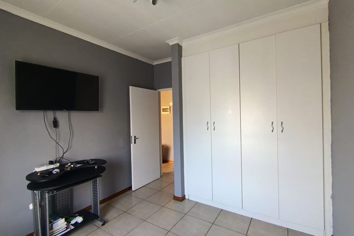 A bedroom featuring tiled flooring, built-in white cupboards, and neutral grey wall paint, providing a functional and clean living space.