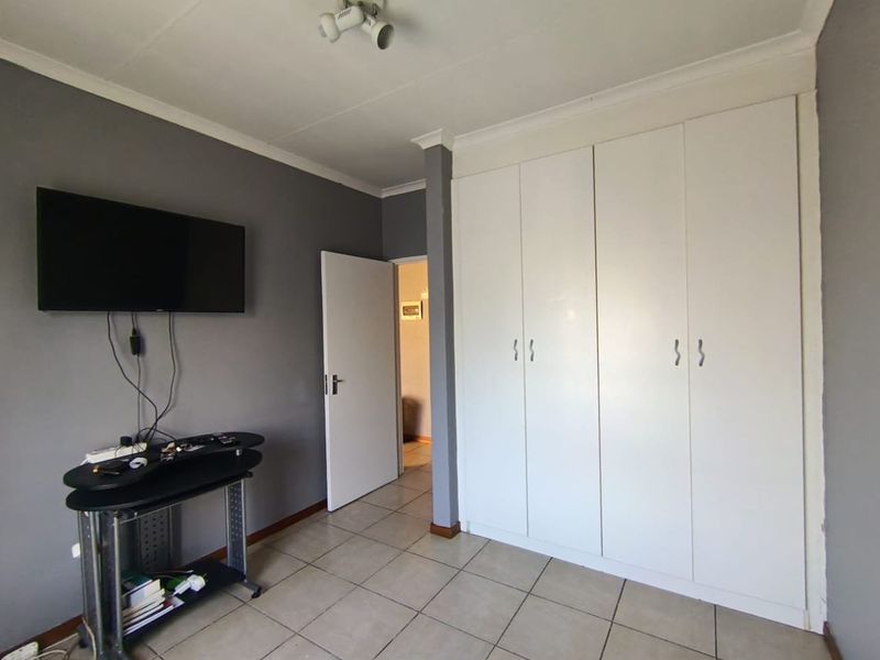 A bedroom featuring tiled flooring, built-in white cupboards, and neutral grey wall paint, providing a functional and clean living space.
