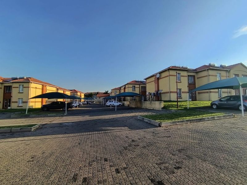 Exterior view of a townhouse complex featuring paved parking areas, covered carports, and multi-story residential units with solar water heating systems.