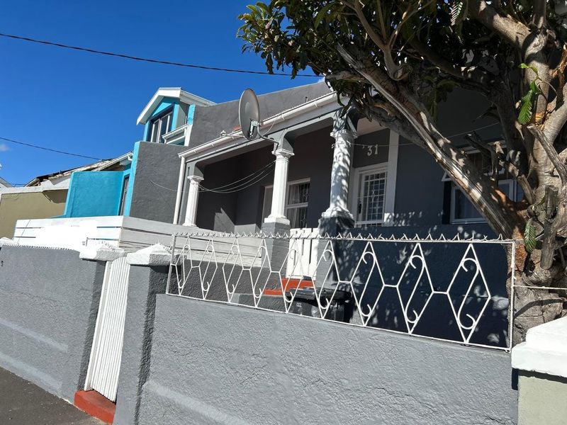 Front elevation of a character home featuring a covered porch with decorative columns, secure boundary wall, and metal fencing.