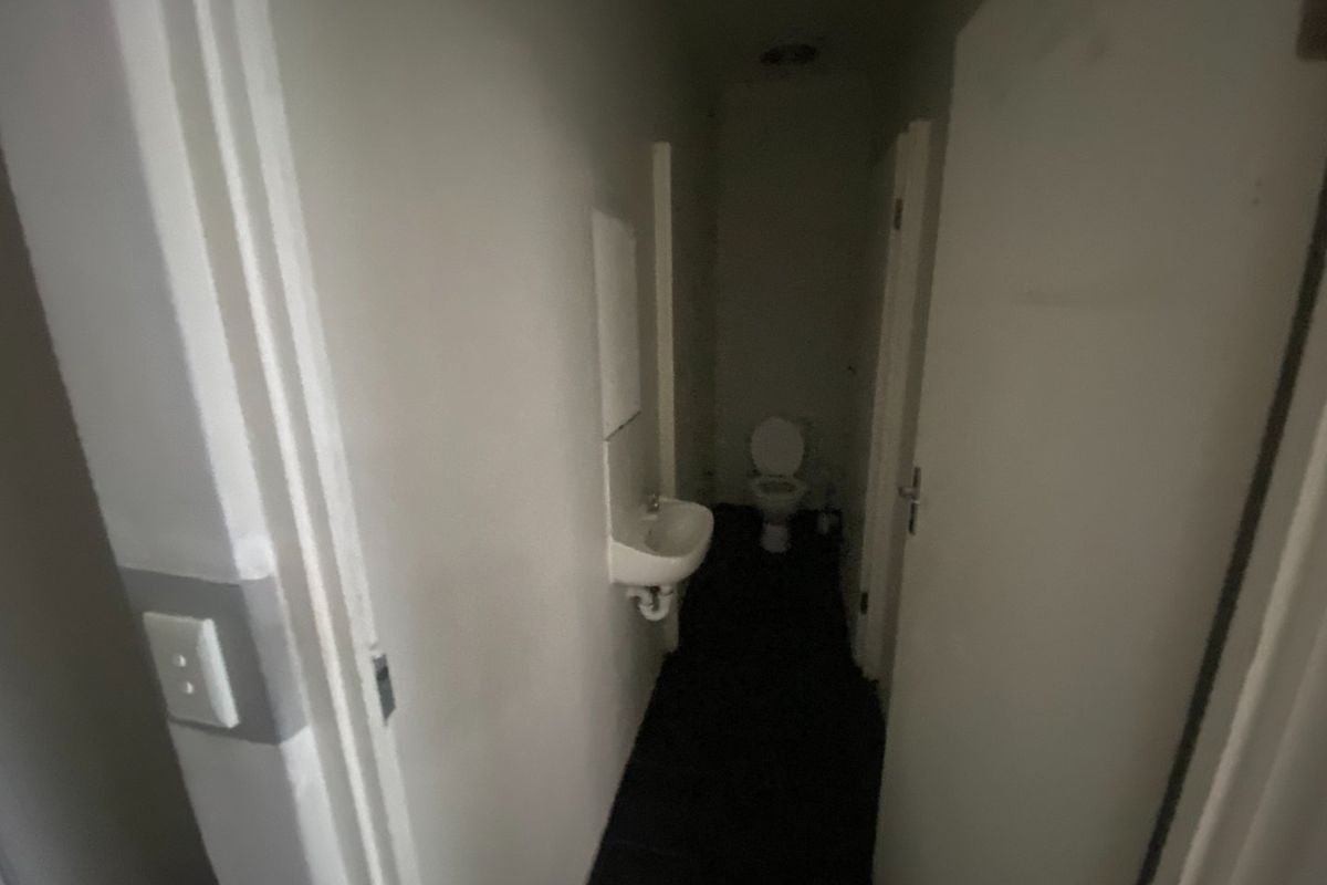 A small, dimly lit bathroom featuring a wall-mounted basin and a toilet, requiring cosmetic updates and improved lighting.