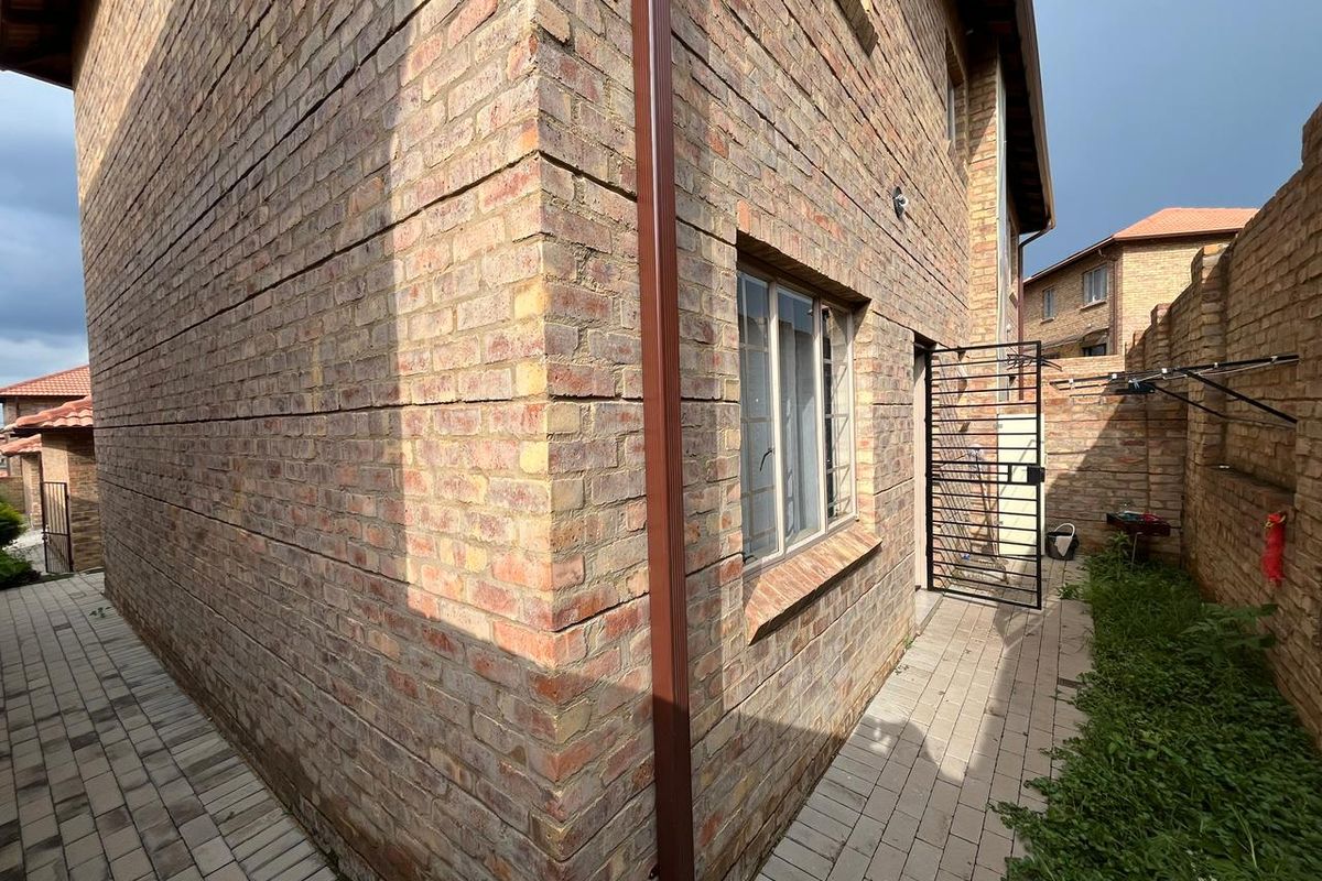 Side view of the property featuring face brick exterior walls, paved pathways, and a metal security gate leading to the rear area.