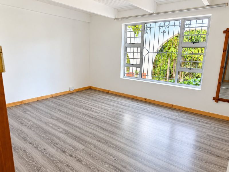 A bright, empty bedroom featuring modern grey laminate flooring, timber skirting boards, and a window fitted with security bars.