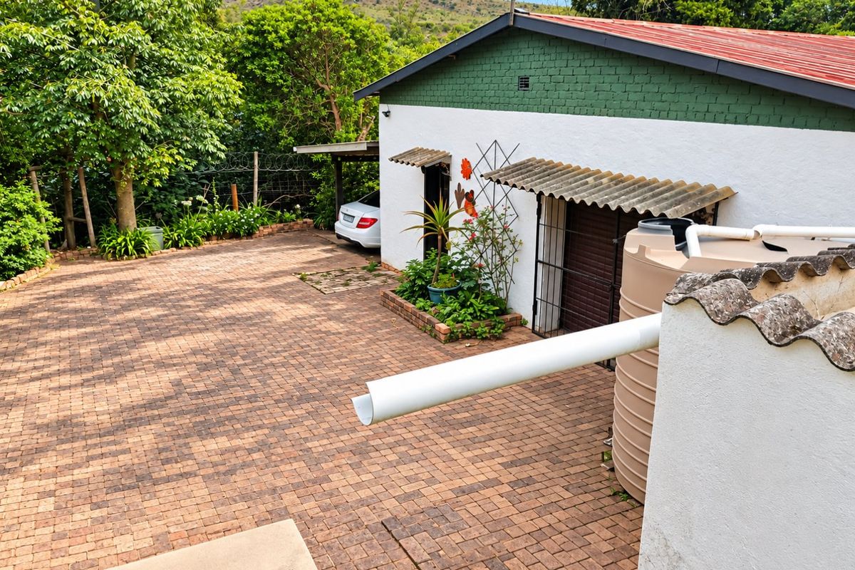Rear exterior view featuring a paved driveway, water storage tank, and a building with a corrugated roof and security gate.