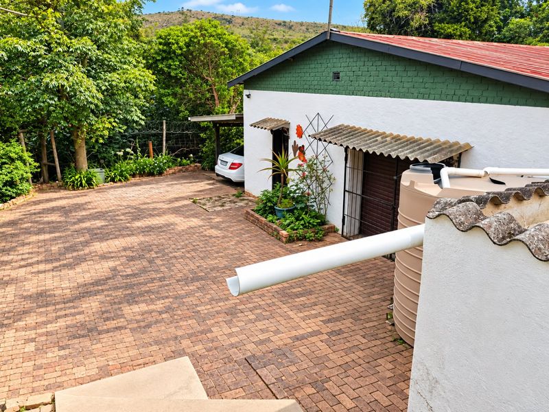 Rear exterior view featuring a paved driveway, water storage tank, and a building with a corrugated roof and security gate.