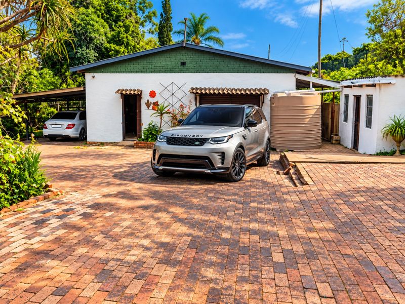 Front exterior view of the property featuring a paved driveway, carport, and a large water storage tank.