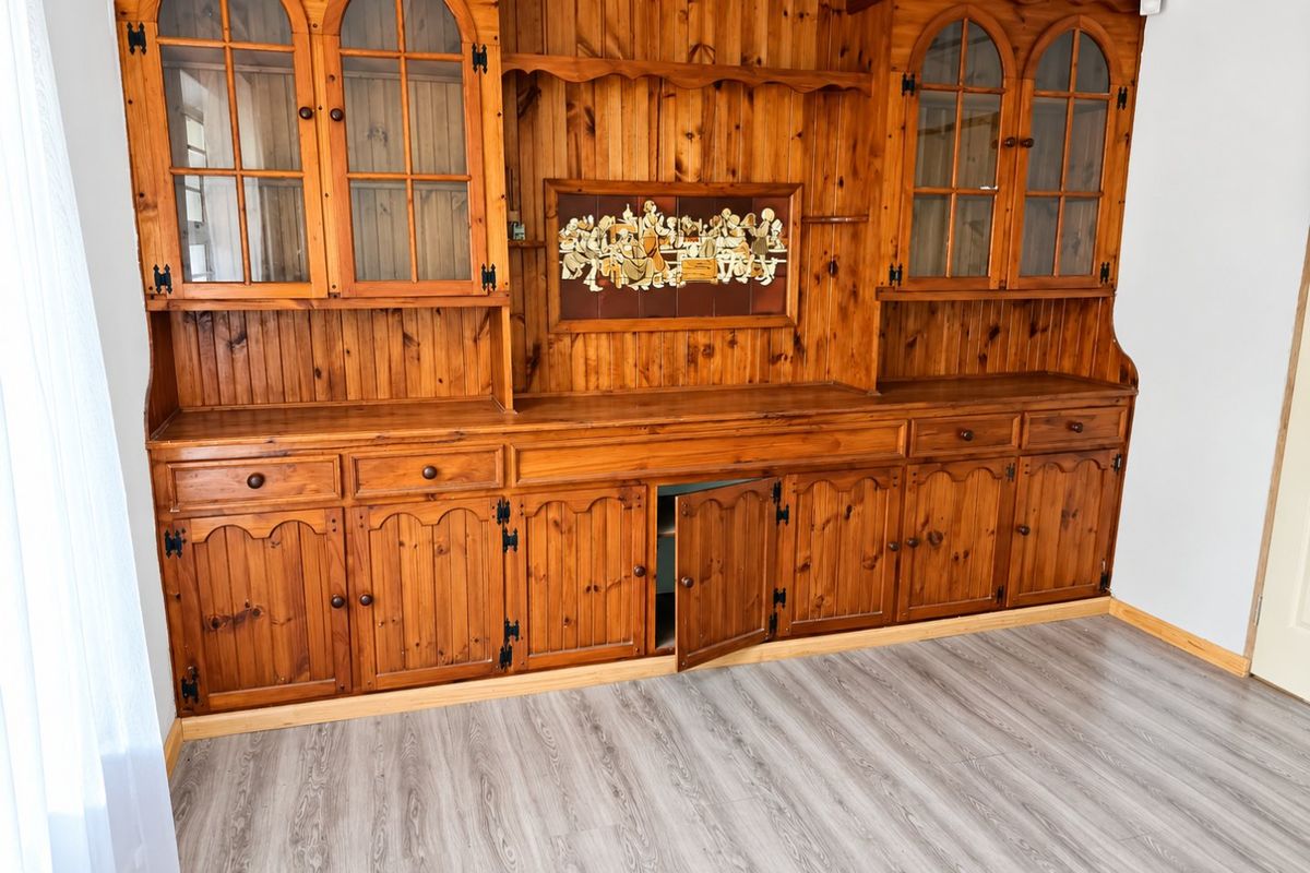 A living area featuring extensive built-in wooden cabinetry and modern laminate flooring, offering significant storage space.