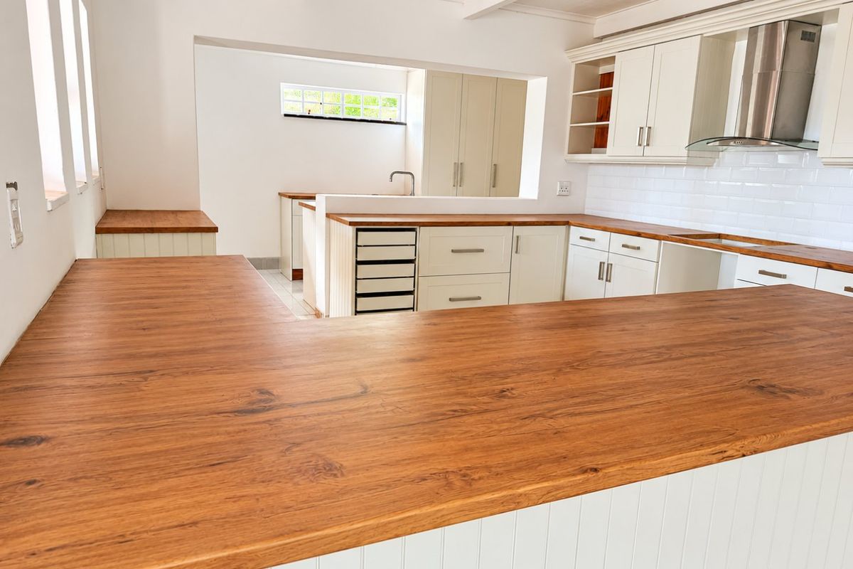 A bright, modern kitchen featuring wooden countertops, white shaker-style cabinetry, a subway tile backsplash, and a stainless steel extractor fan.