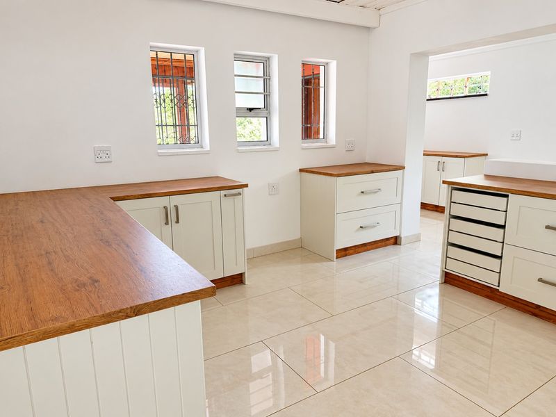 A clean, modern scullery or utility area featuring ample built-in cabinetry, wooden countertops, and polished tiled flooring with natural light from multiple windows.