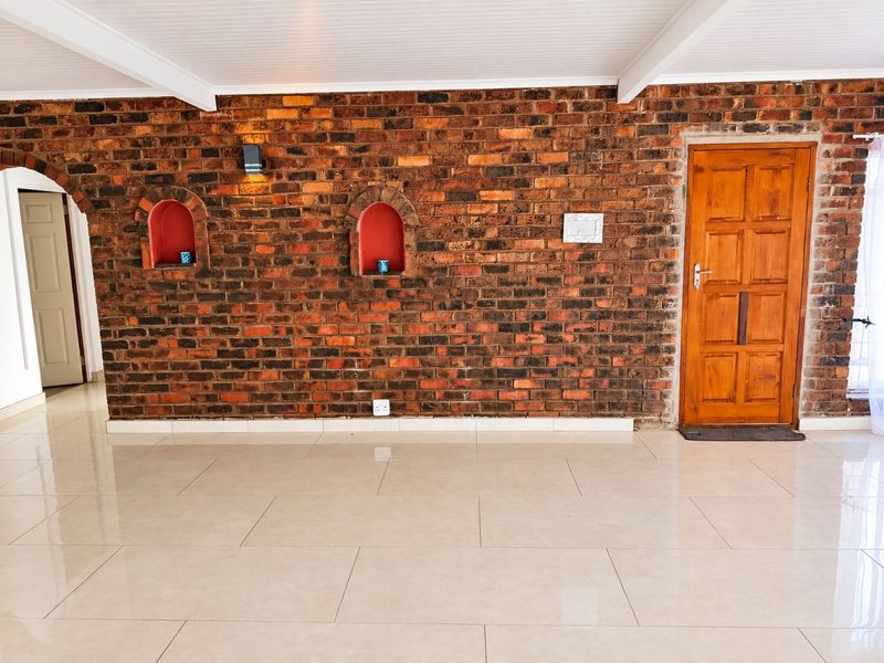 Spacious living area featuring a prominent exposed brick feature wall with arched niches, neutral tiled flooring, and a classic timber entrance door.
