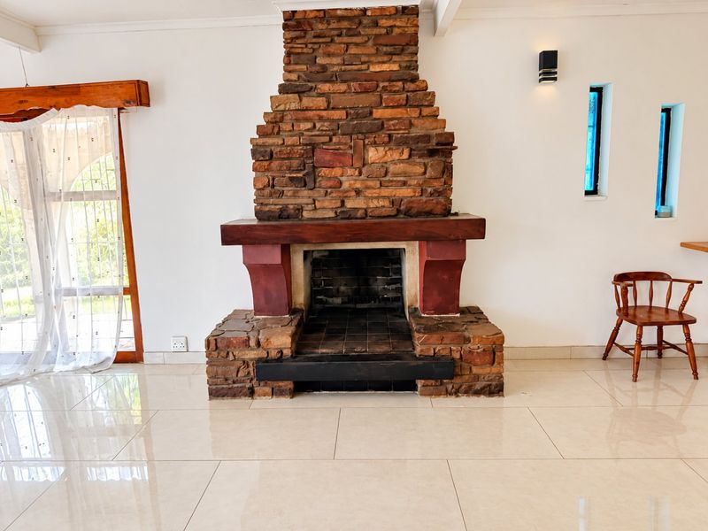 Spacious living area featuring a prominent rustic brick fireplace with a wooden mantelpiece and polished tiled flooring.