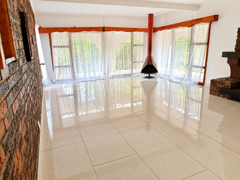 Spacious living area featuring polished tiled floors, an exposed brick feature wall, and a unique freestanding fireplace with large glass doors leading outside.