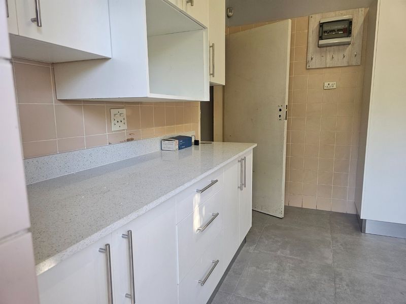 A functional kitchen area featuring modern white cabinetry, quartz countertops, and neutral tiled finishes, providing a clean and practical workspace.