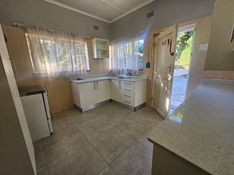 Functional kitchen featuring stone countertops, built-in cabinetry, tiled splashbacks, and direct access to the rear exterior area.