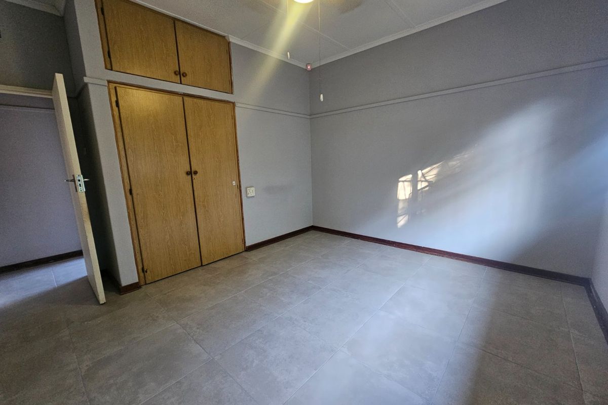 An empty bedroom featuring neutral tiled flooring, built-in wooden cupboards with overhead storage, and a ceiling fan.
