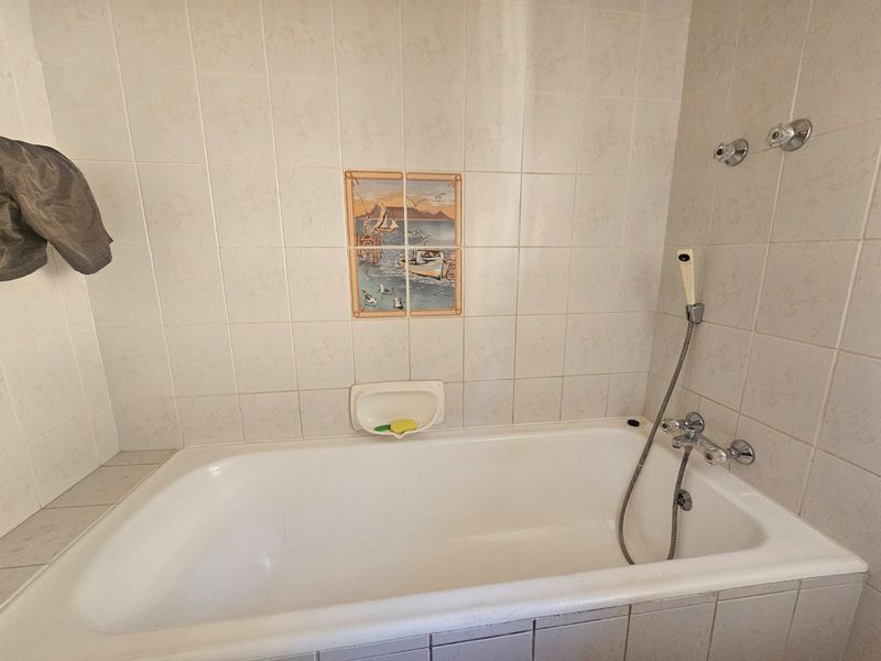 A functional bathroom featuring a built-in bathtub with wall-mounted shower fixtures and decorative ceramic wall tiling.
