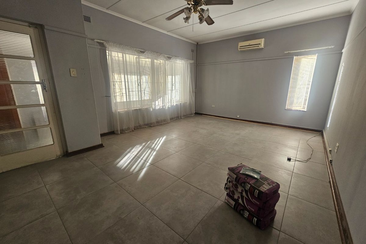 Spacious, empty living room featuring neutral tiled flooring, a ceiling fan, and a wall-mounted air conditioning unit.