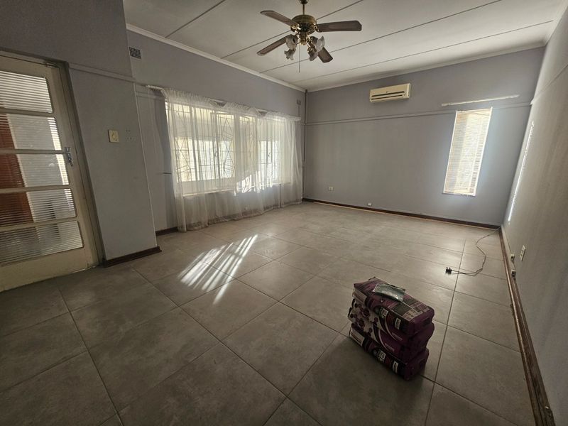 Spacious, empty living room featuring neutral tiled flooring, a ceiling fan, and a wall-mounted air conditioning unit.