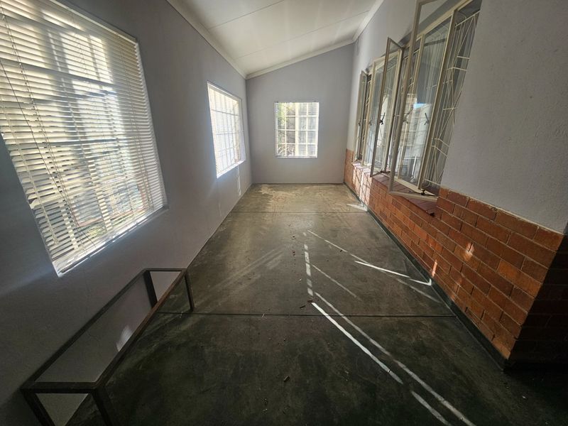 An enclosed sunroom or patio area featuring concrete flooring, brick wall detailing, and multiple windows with security bars and blinds.